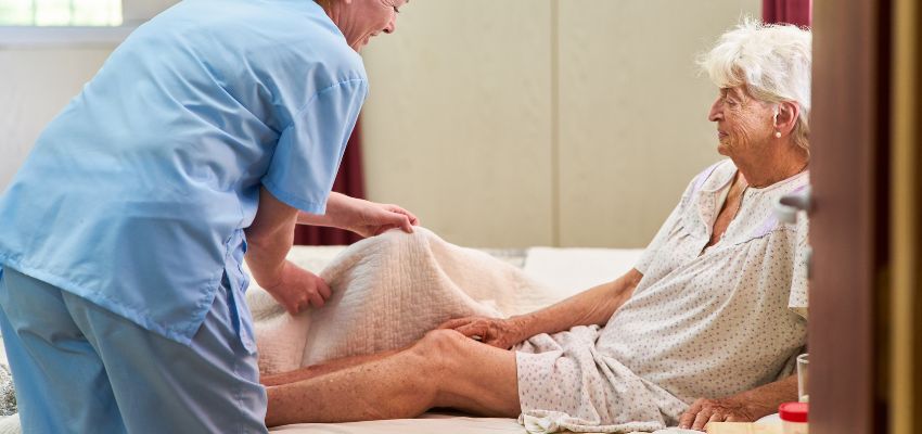 The nurse helps the patient to change her position to prevent pressure ulcers.